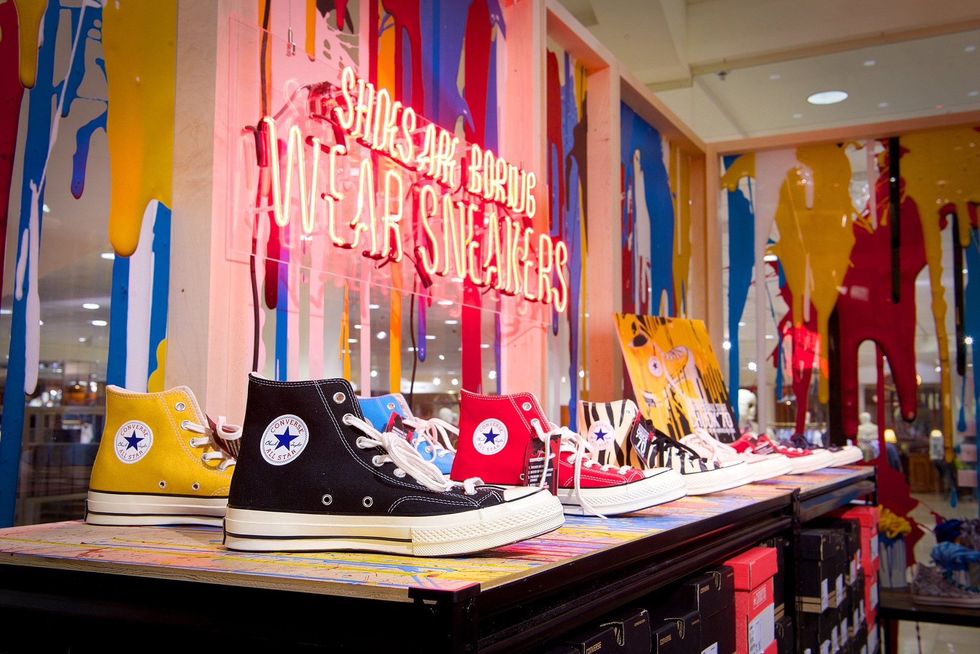 Converse All Stars shoes on top of a counter over a neon sign. 